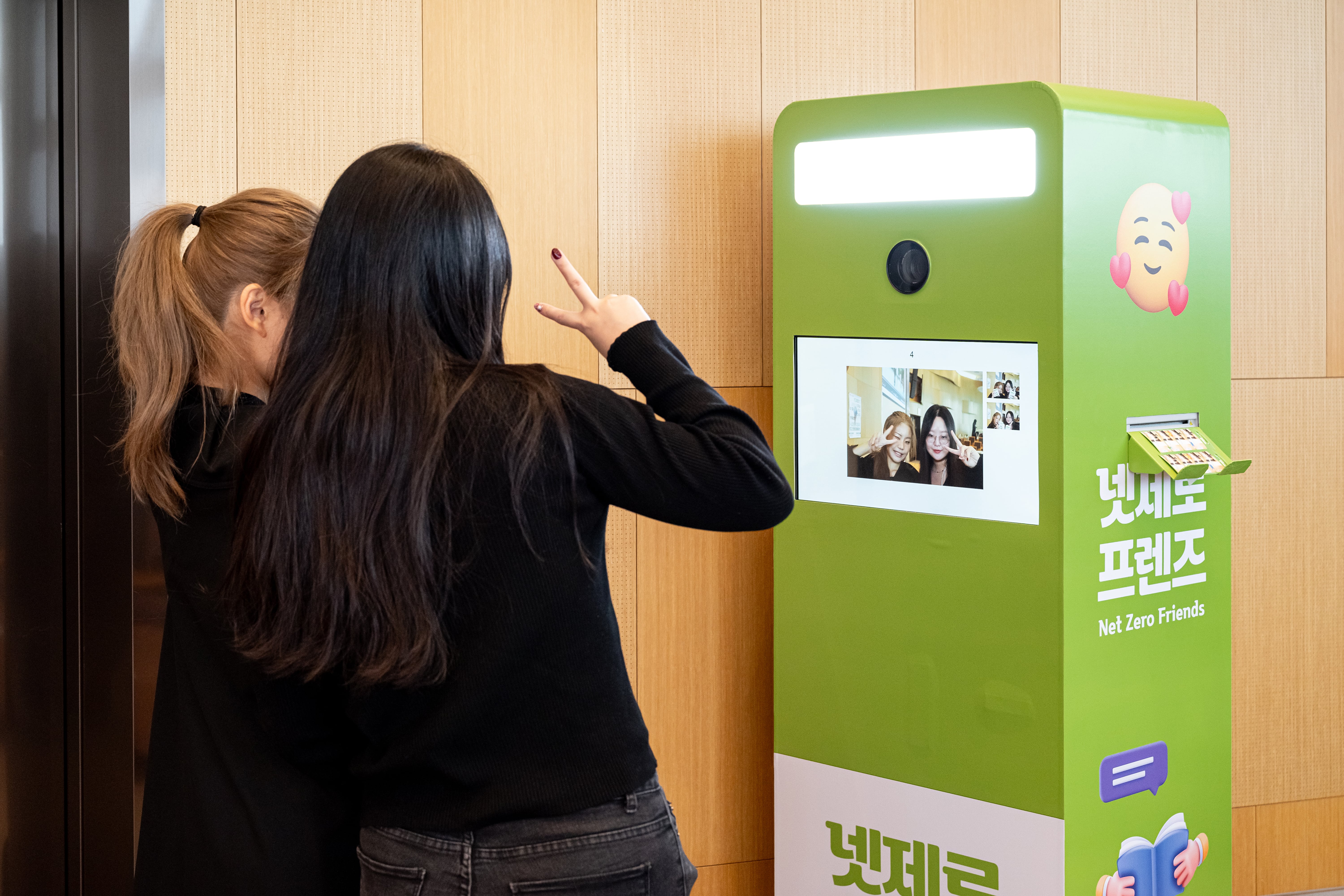 여성 두명이 사진찍는 기계 앞에서 브이를 하며 사진을 찍는 모습